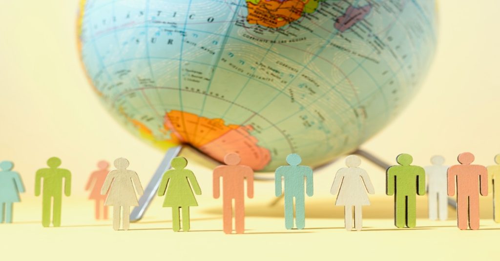 People from various backgrounds stand around a globe, highlighting the benefit of access to global talent in remote video production.