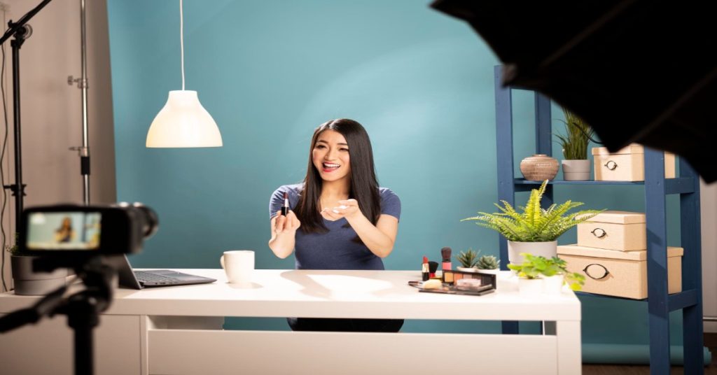 A woman poses in front of a camera and a table with a phone, emphasizing the concept of sustainable video production.