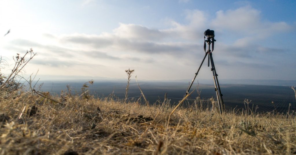 A tripod on a hilltop overlooking the sky, symbolizing sustainable video production and set design.