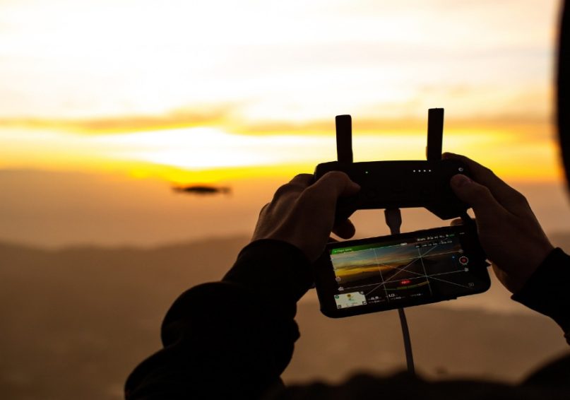 Drone Videography A person holds a smartphone while a drone hovers in the background, illustrating drone videography techniques.