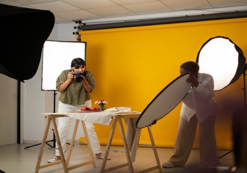 Two people in a photo studio with yellow walls, demonstrating lighting techniques for corporate videos.