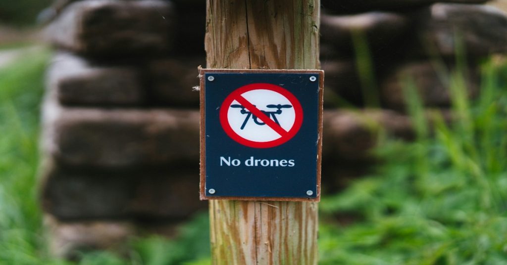 A wooden post displays a no drones sign, indicating that drone videography is prohibited here.