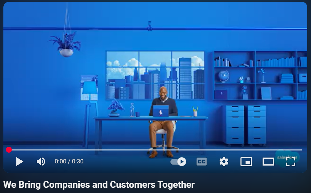 A man is seated at a desk with a blue wall behind him, illustrating lighting techniques in a Salesforce corporate video.