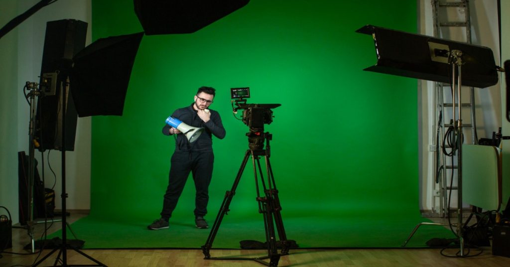 A man is positioned in front of a green screen, illustrating the use of lighting techniques in video production.