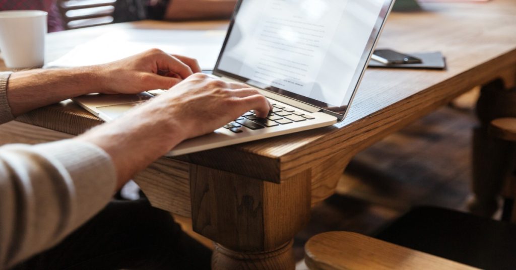 A person typing on a laptop at a table, engaged in script writing and storyboarding for the project.