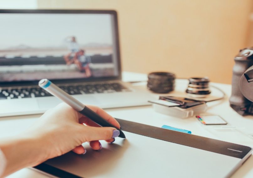 A person using a pen to draw storyboarding ideas on a laptop for video production.